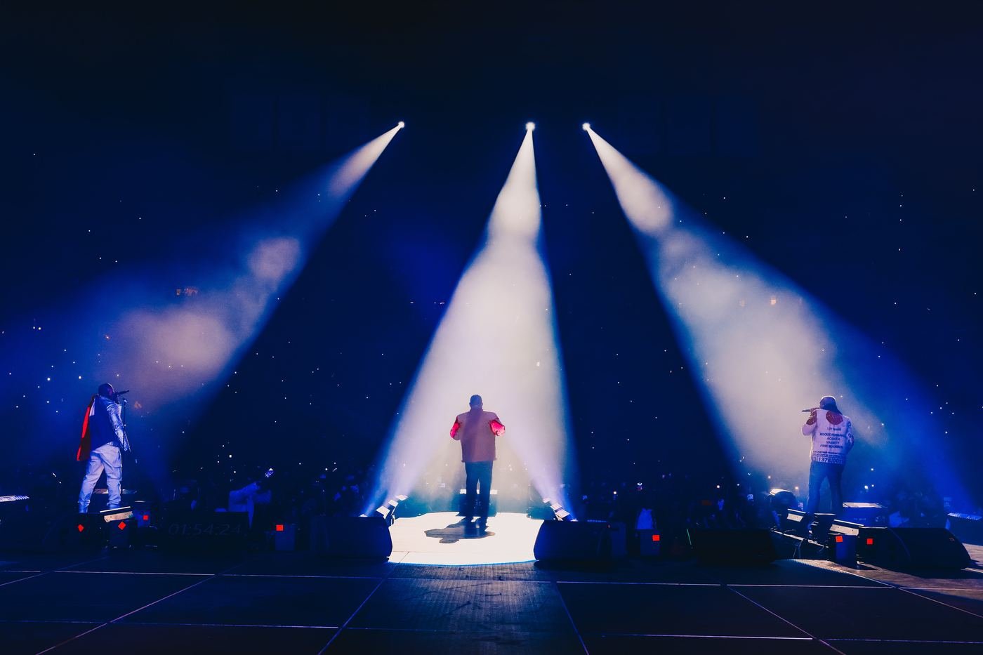 Band silhouetted on stage under three spotlight beams