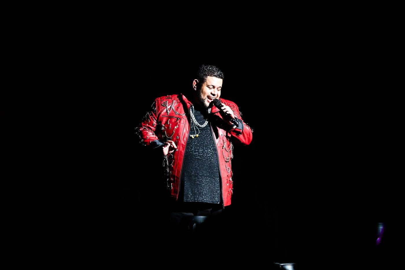 Mickael Guirand performing solo in a red jacket under spotlight
